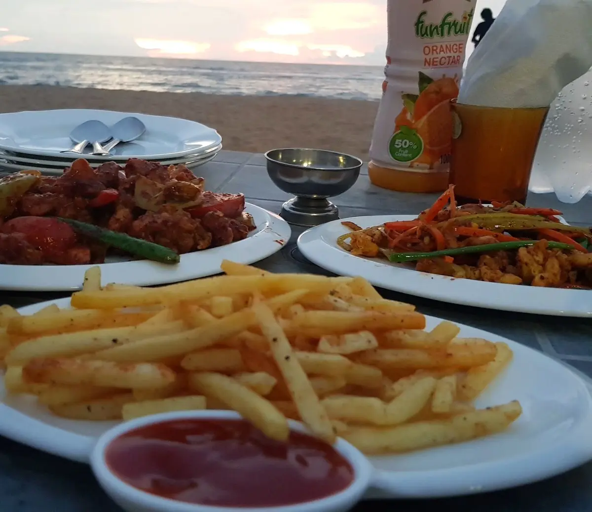 Devilled dishes and a plate of chips on a beachside table at sunset