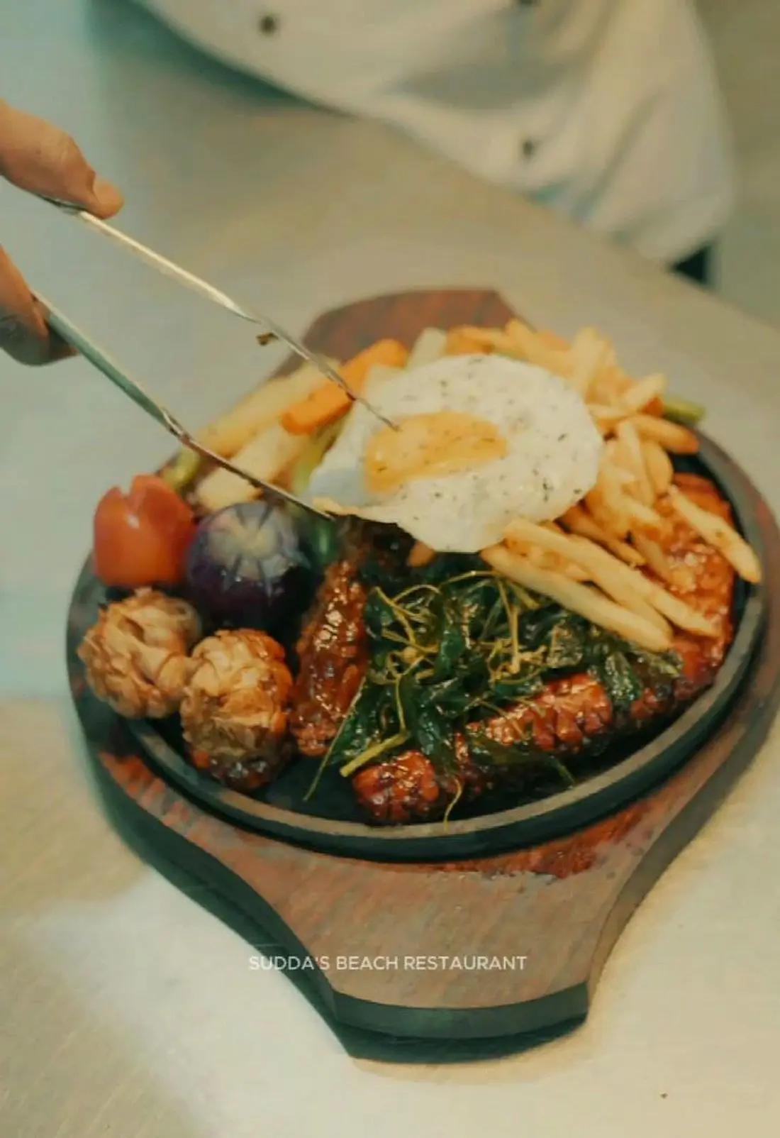 Sizzling platter with devilled meat, fried egg, chips and vegetables being served