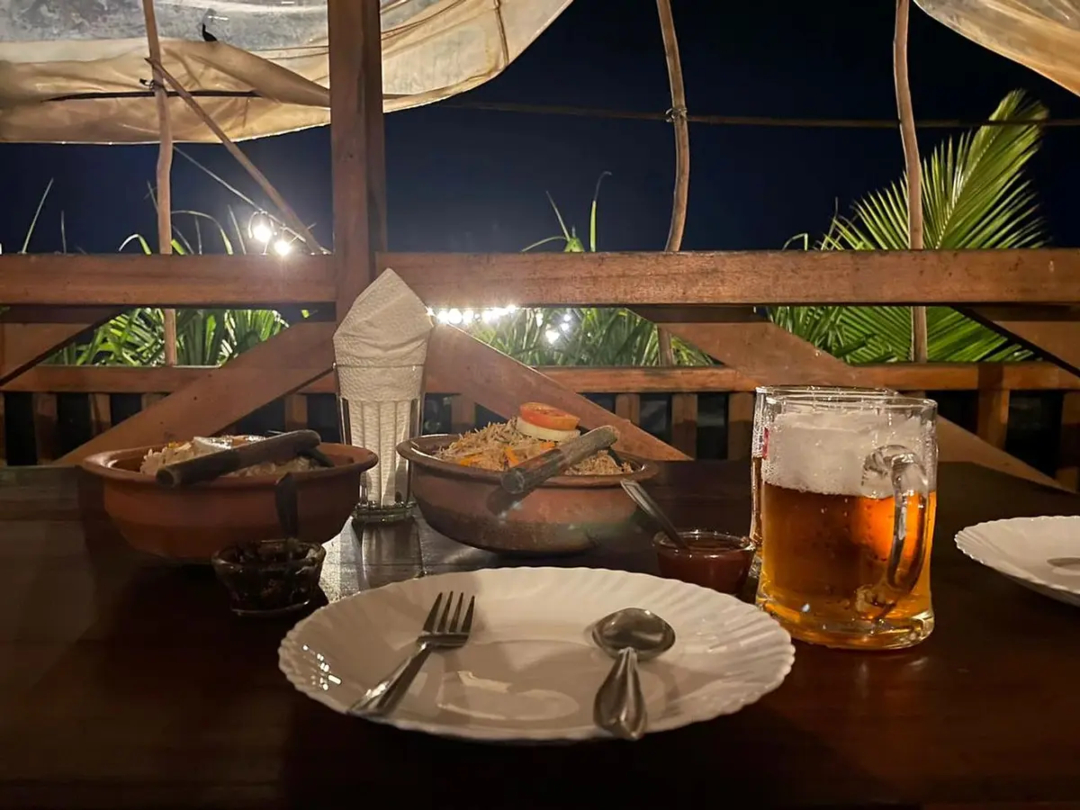 Clay pots of rice and curry with a cold drink on a timber table at night