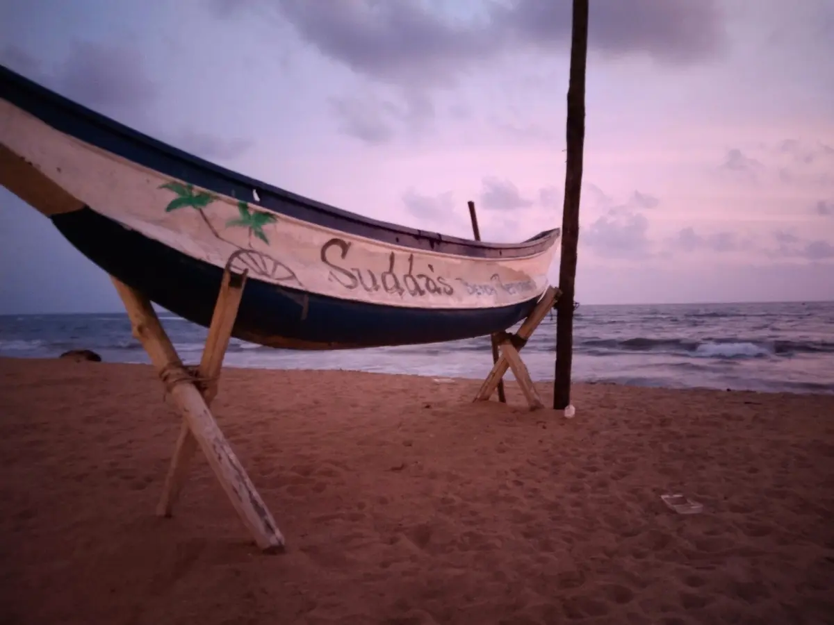 Sudda's painted fishing boat resting on the sand at dusk, the sea behind it