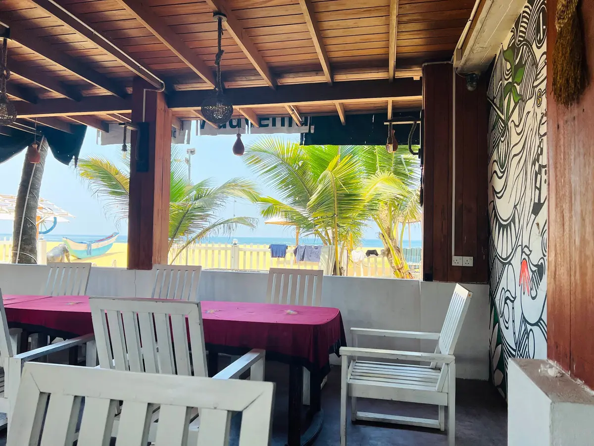 Covered terrace with white chairs and a sea view between palm trees
